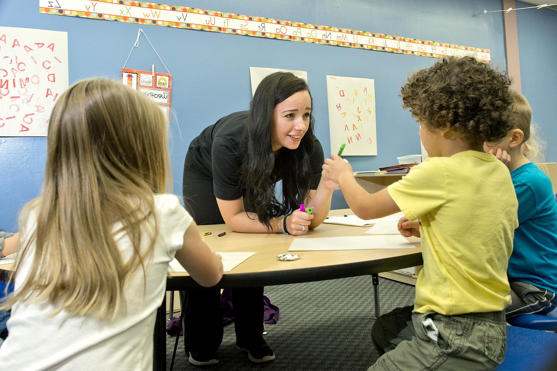 student leaning over to help three small children